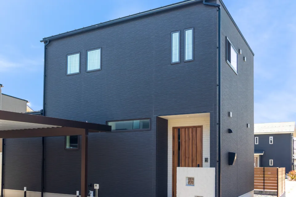濃いグレーの外壁と木製ドアの2階建て住宅